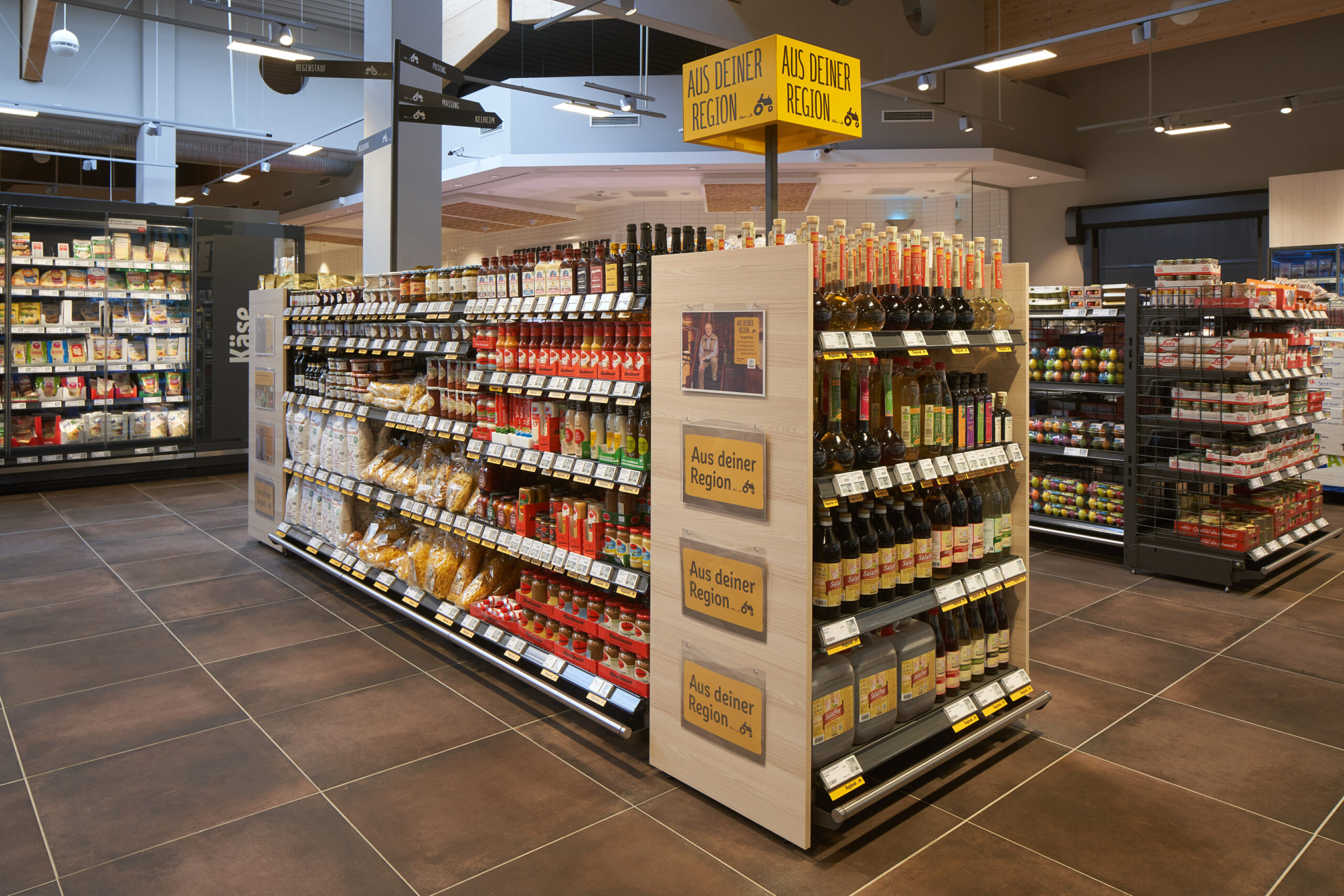 Regal in Raummitte mit regionalem Wein und Soßen in Flaschen. Auf dem Regal ist ein Schild, dass auf die Regionalität der Waren hinweist.